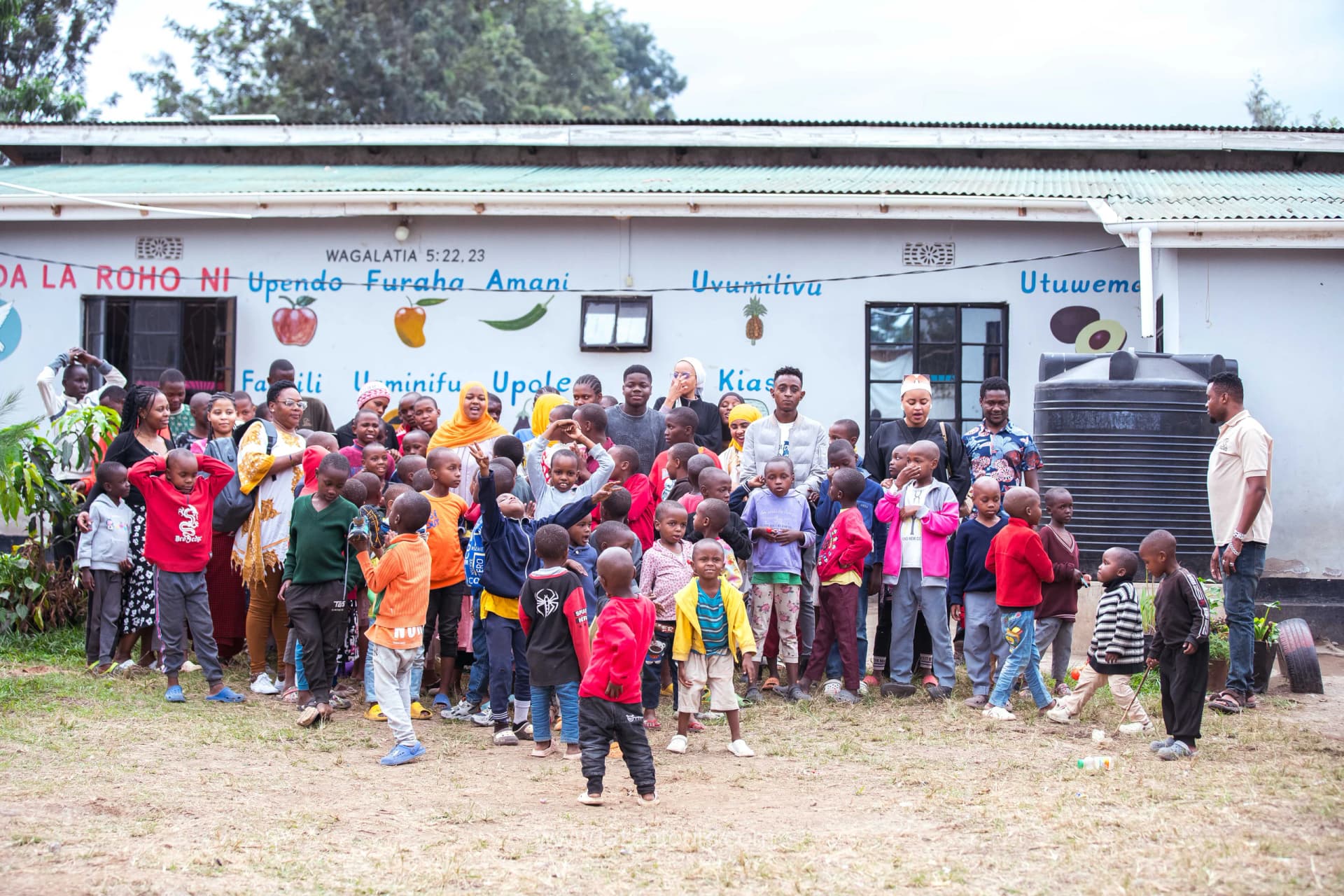 The Tazan team with children and families outside a school building at a community day